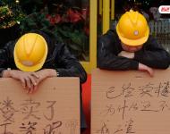 2012年12月25日，廣東中山，火炬開發(fā)區(qū)的多名建筑工人討要工作一年多的血汗錢一籌莫展，一些工人干脆將鋪蓋卷搬到了售樓部，并在門口搭起灶臺煮飯，希望以這種方式討回工錢。圖為在銷售中心門外，工人舉牌討薪。吳進/視覺中國